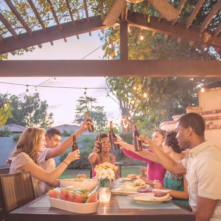 Friends sitting at a table outside gesturing for a 'cheers'.