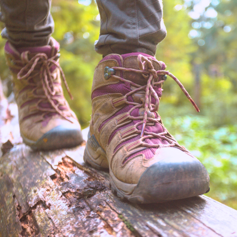 View of someone's hiking boots as they walk across a log.