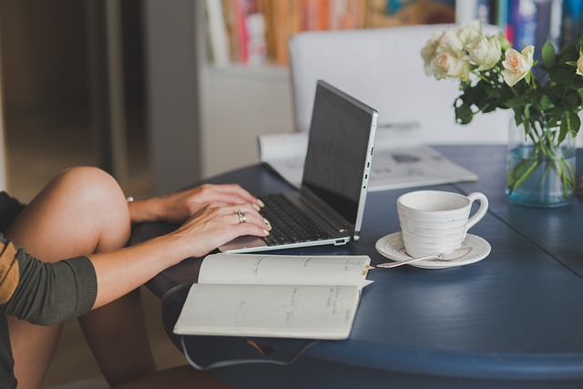 Women working on a computer with a journal and tea on the table.